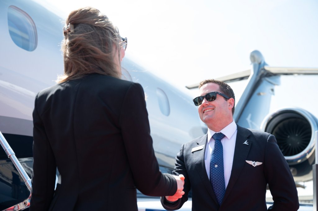 Representante de una compañía de vuelos chárter saludando a un pasajero junto a un jet privado